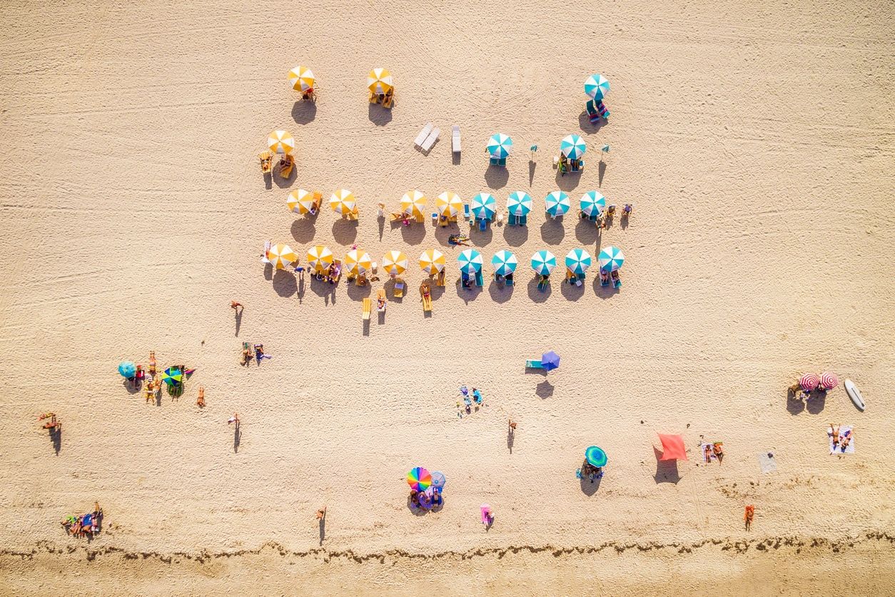Aerial view of colorful beach umbrellas and people on sandy shore.