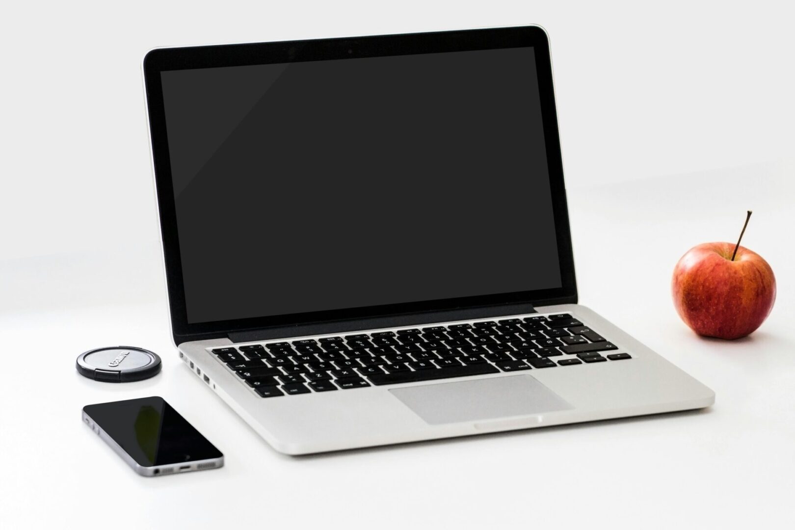A laptop with a smartphone and glasses on a white surface.