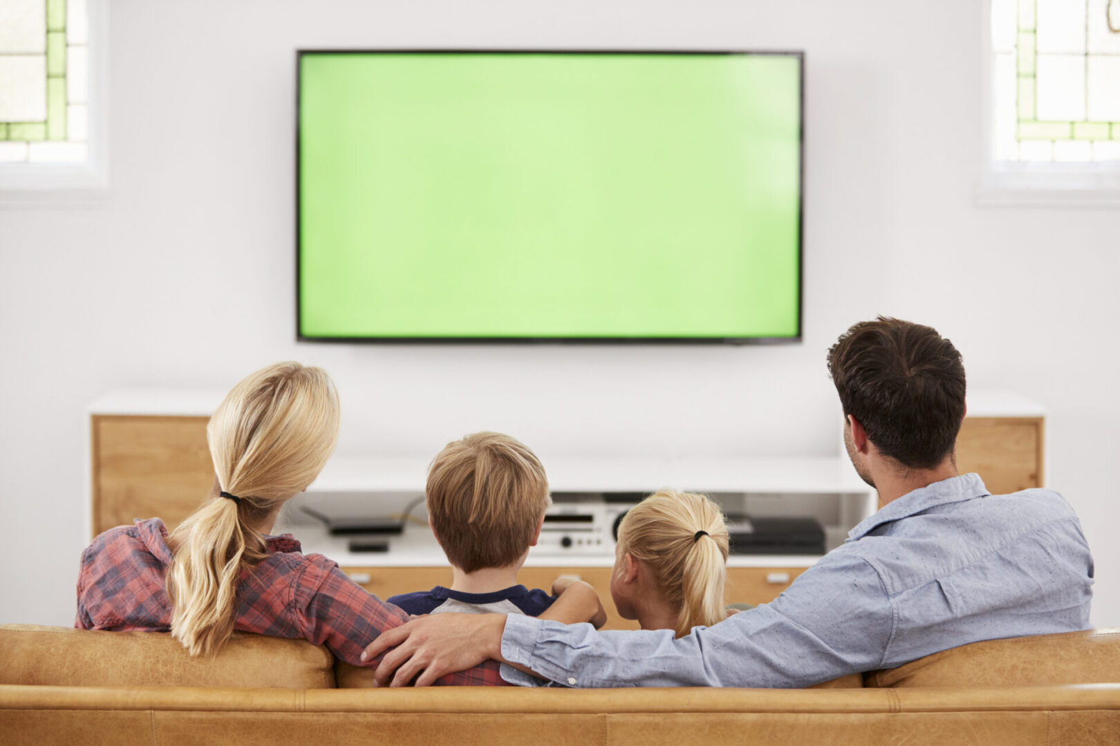 Family of four watching a large TV with a green screen.