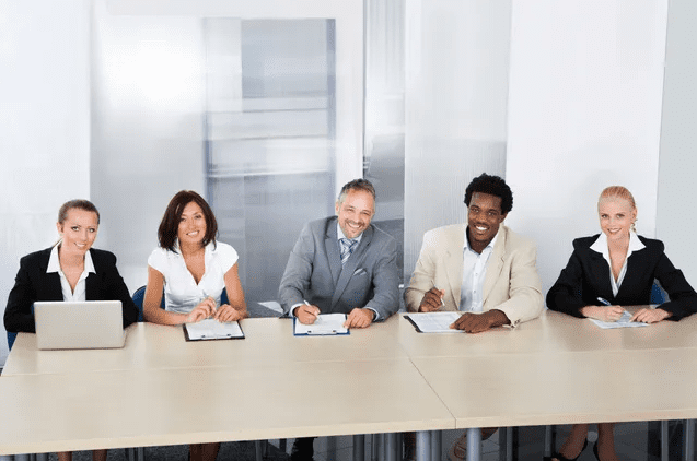 Diverse professionals smiling at a meeting table with documents.