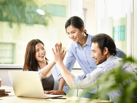 Three colleagues celebrating success with a high-five in an office.
