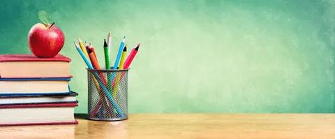 Colorful pencils in a metal holder on a wooden desk against a green wall.